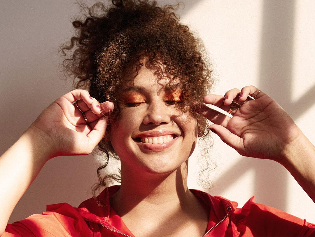 Close-up image of a model with curly hair smiling and posing while eyes closed Desktop
