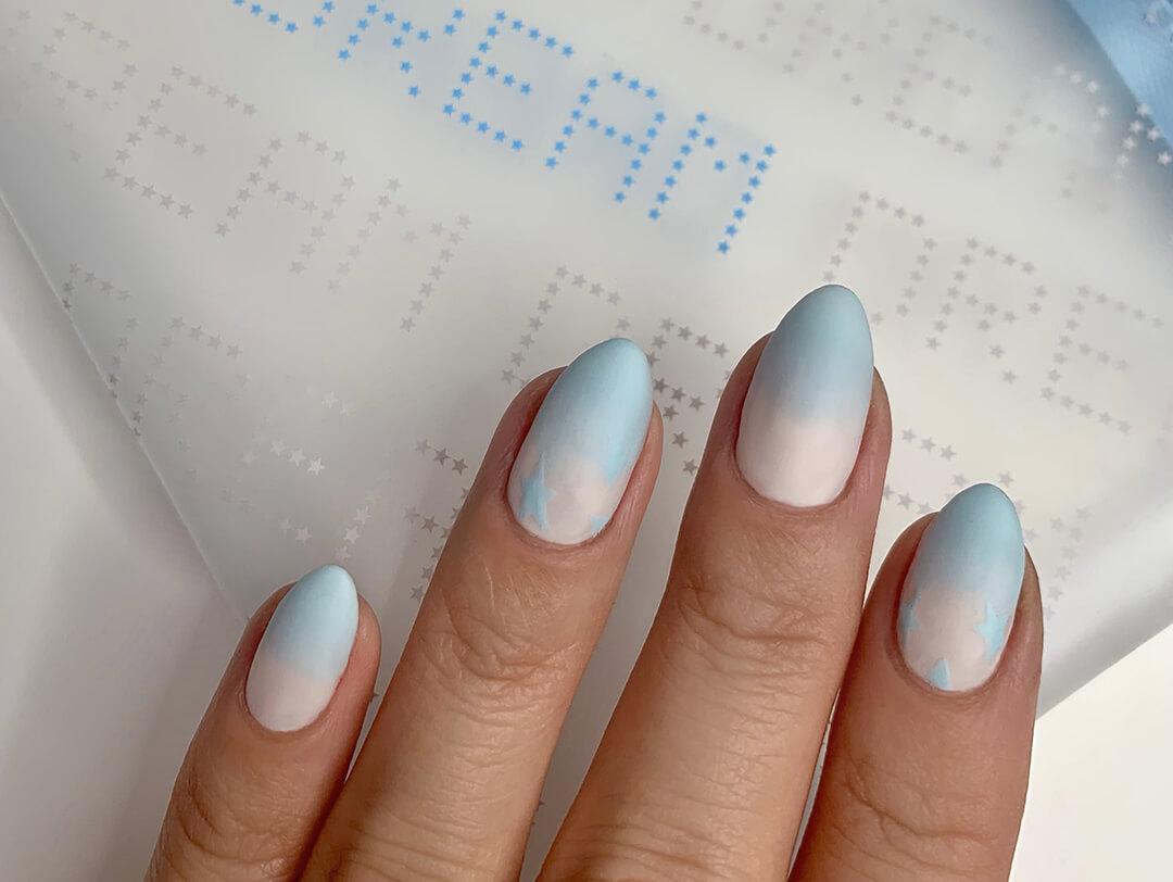 Close-up of a model's nails with blue and white ombre nail art touching the January 2021 IPSY Glam Bag