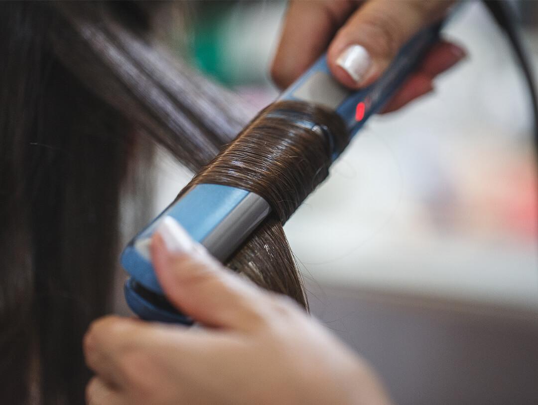 Close-up image of a hairstylist's hands using a flat iron to curl a woman's dark hair Desktop