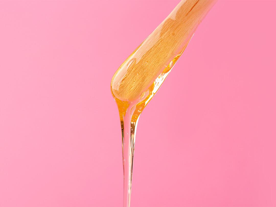 Close-up image of a spatula with melted wax on pink background Desktop