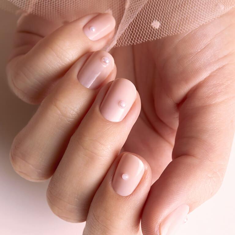 An image of a model's hand with pearl accented mani holding nude pink tulle Desktop