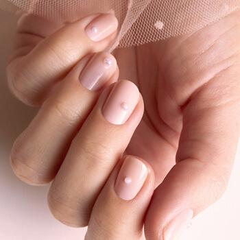 An image of a model's hand with pearl accented mani holding nude pink tulle Mobile