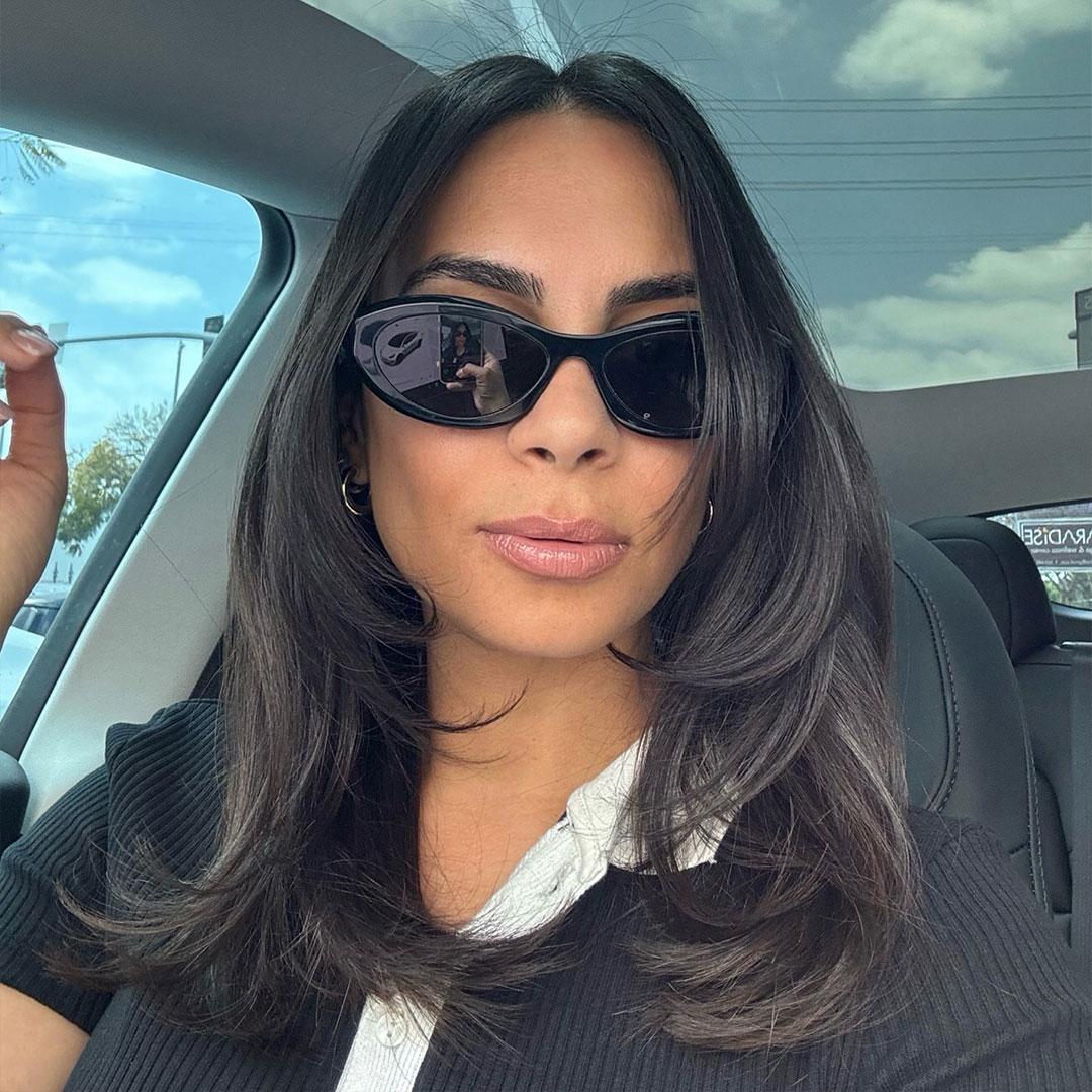 A woman sitting in a car seat, wearing black sunglasses, pouting her lips, and showing off her beautiful black hair Desktop