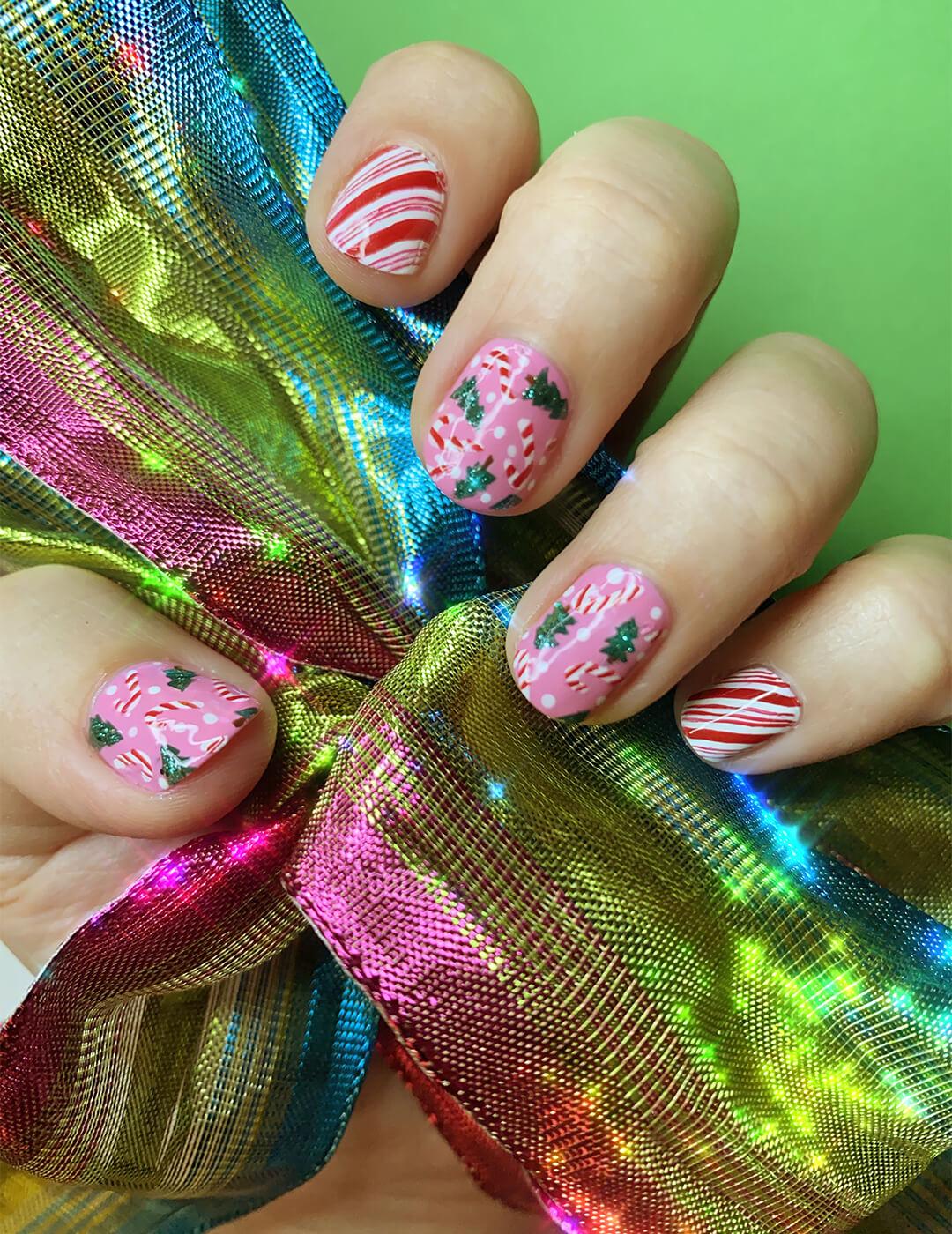Close-up image of a model's hand with a peppermint, candy cane, and Christmas tree themed nail art mani holding a shiny rainbow colored ribbon Mobile