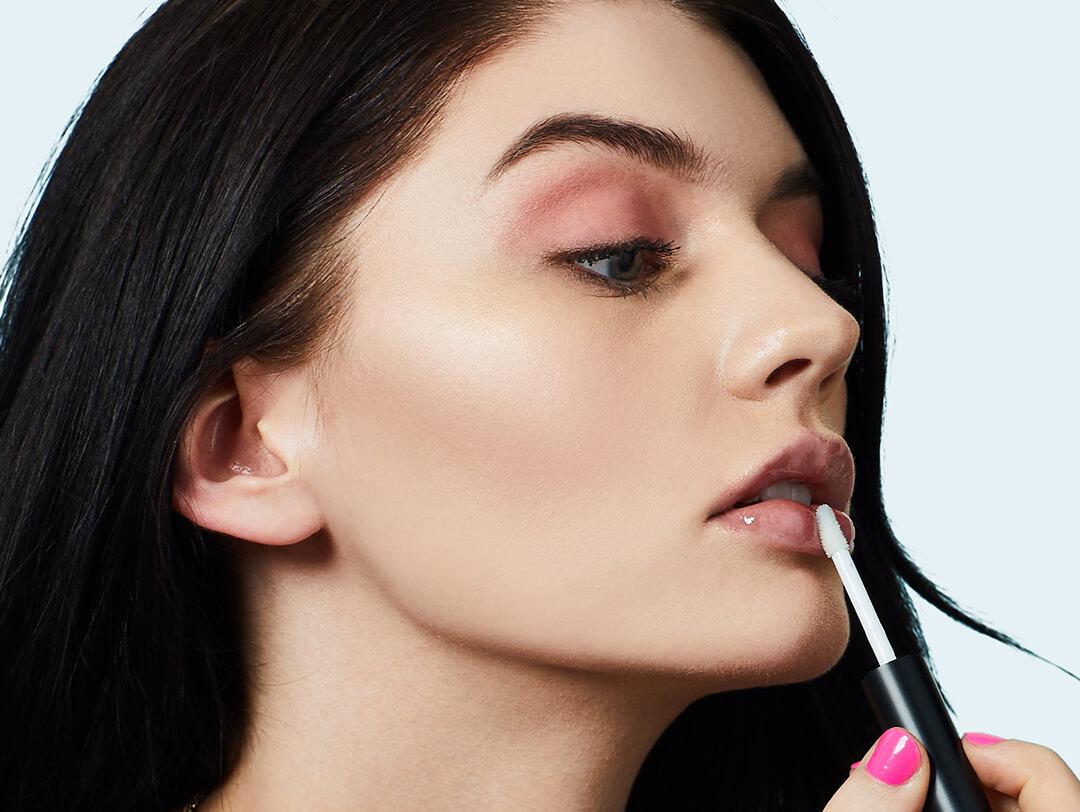 A photo of a model applying clear lip gloss on her lips
