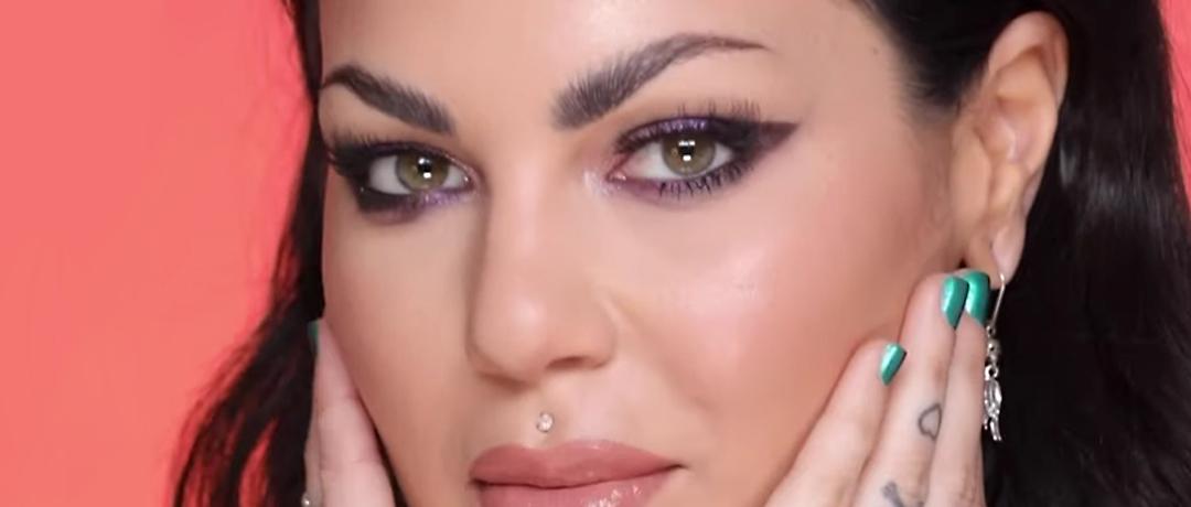 Bailey Sarian rocking a purple eyeshadow look posing on coral background