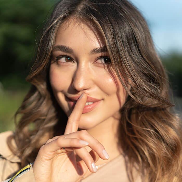 A close-up image capturing a smiling woman with her finger resting on the top of her lips Mobile