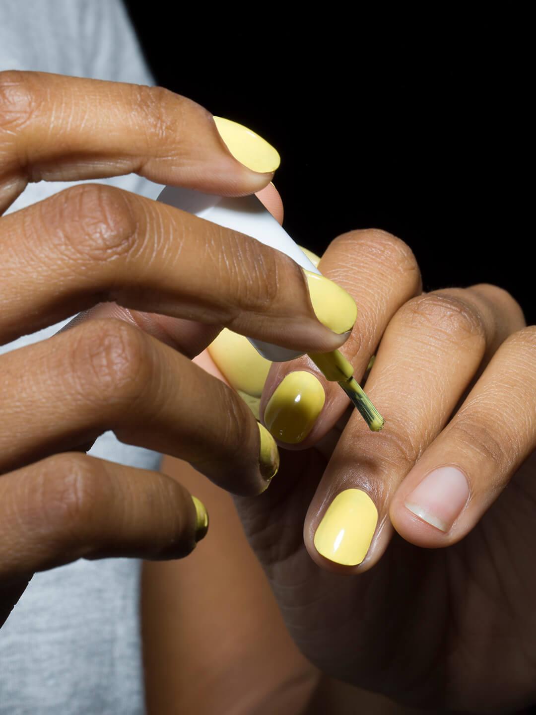 Close-up of young mixed-race woman applying yellow nail polish Desktop