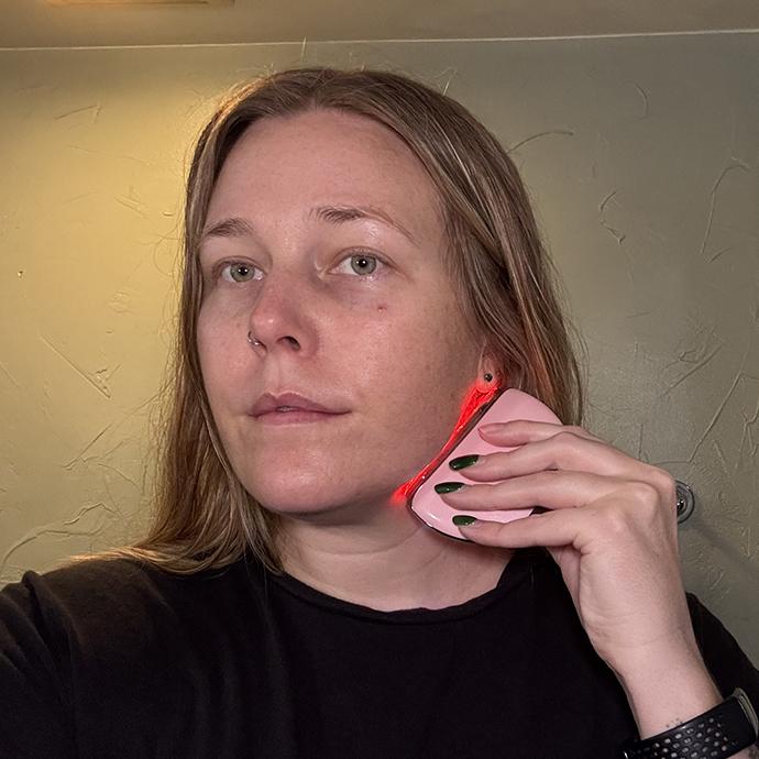 Person using a red light facial skincare device along the jawline, illustrating a beauty self-care routine focused on skin maintenance and wellness