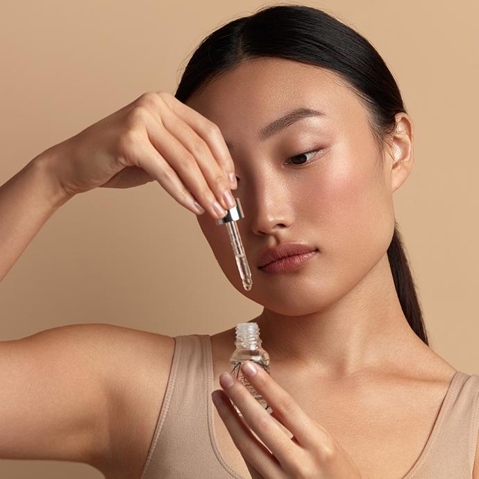 Woman Applying Serum on Face. Asian Girl Holding Essential Oil And On It. Beautiful Model Moisturizing Derma With Natural Vitamin E, Serum Collagen And Hyaluronic Acid