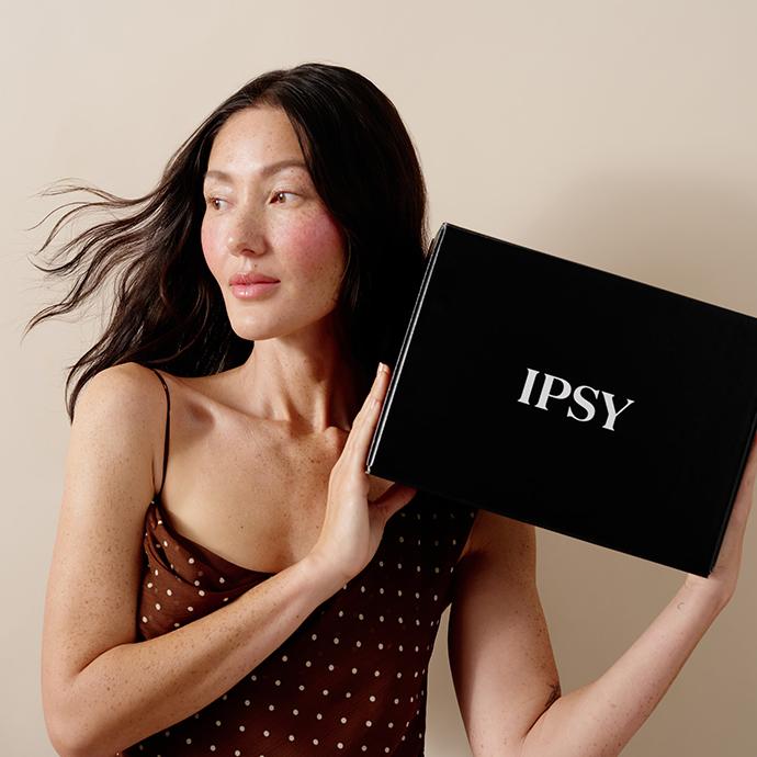 Model holding IPSY Ultimate beauty box, showcasing the black subscription box with a glowing, natural makeup look.