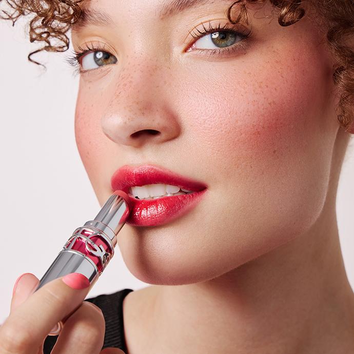 Close-up of model applying glossy red lipstick with softly diffused edges, illustrating the blurred lip trend with a modern, soft-focus finish