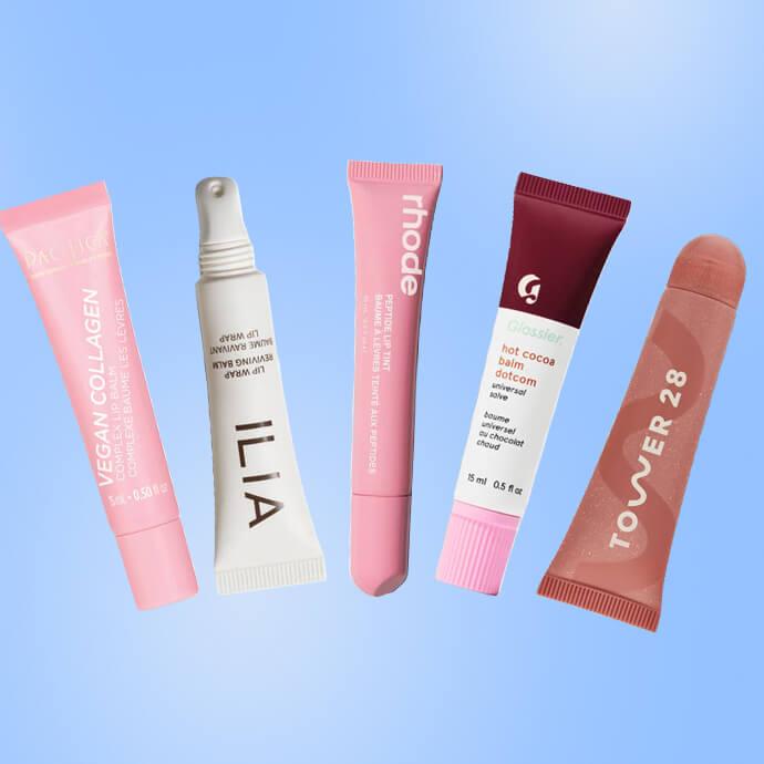 A row of colorful skincare tubes and a capsule-shaped product from brands Pacifica, Ilia, Rhode, Glossier and Tower 28 against a light blue background