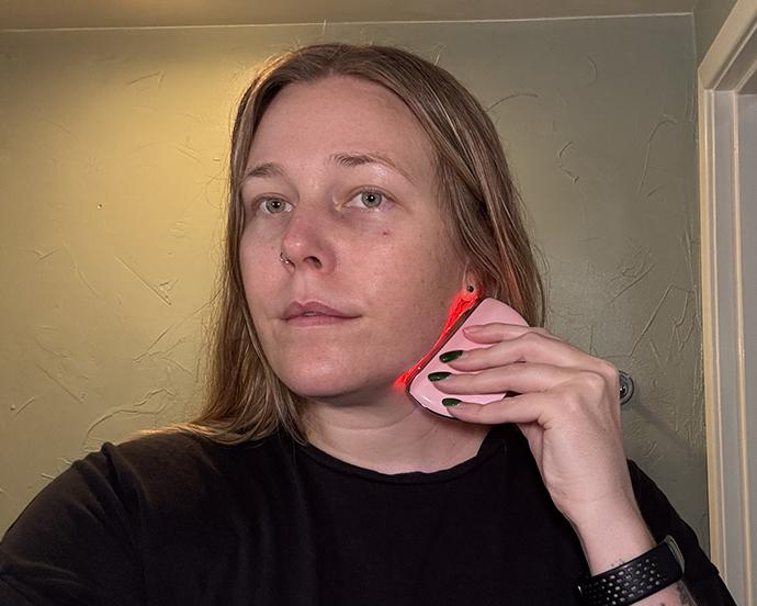 Person using a red light facial skincare device along the jawline, illustrating a beauty self-care routine focused on skin maintenance and wellness
