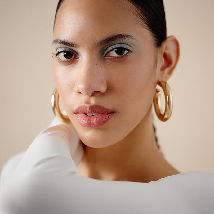Model with slicked-back hair wearing frosted blue eyeshadow, glowing skin, and glossy lips for a modern soft glam makeup look