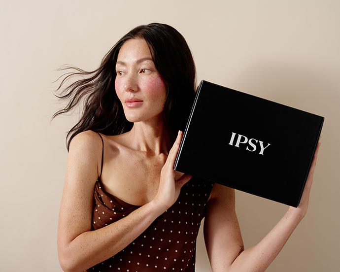 Model holding IPSY Ultimate beauty box, showcasing the black subscription box with a glowing, natural makeup look.