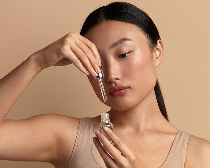 Woman Applying Serum on Face. Asian Girl Holding Essential Oil And On It. Beautiful Model Moisturizing Derma With Natural Vitamin E, Serum Collagen And Hyaluronic Acid