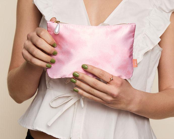 Model holding the April 2026 IPSY Glam Bag, a pink watercolor makeup pouch with a pearl zipper pull.