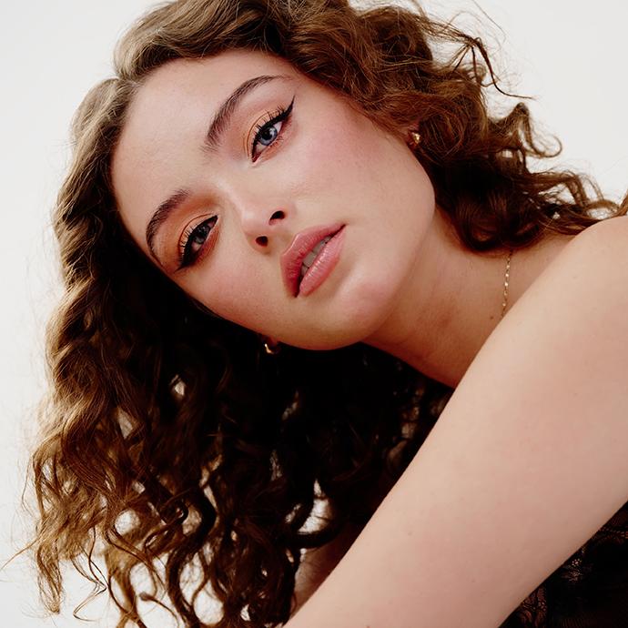Model with natural air-dried curly hair and soft makeup, showcasing effortless texture and a low-maintenance hair routine