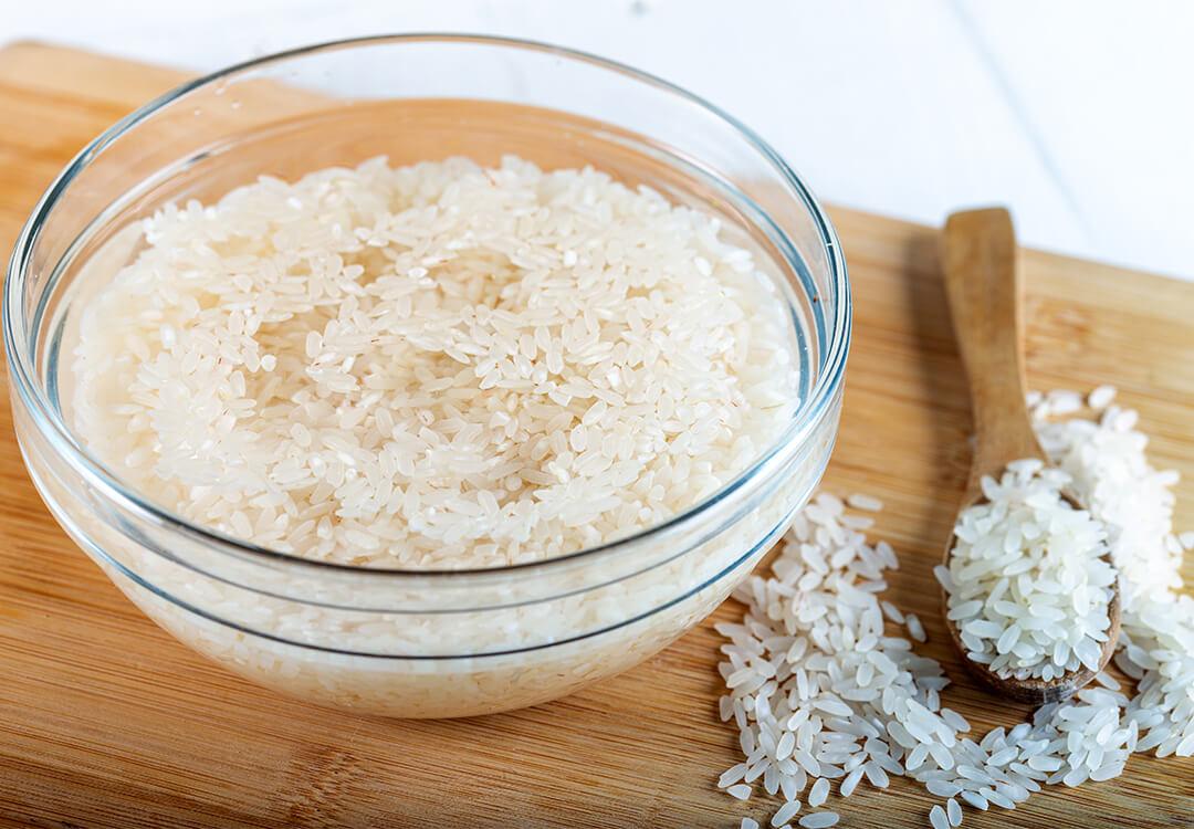 Rice soaked in a bowl of water and wooden spoon full of rice on wooden background Desktop