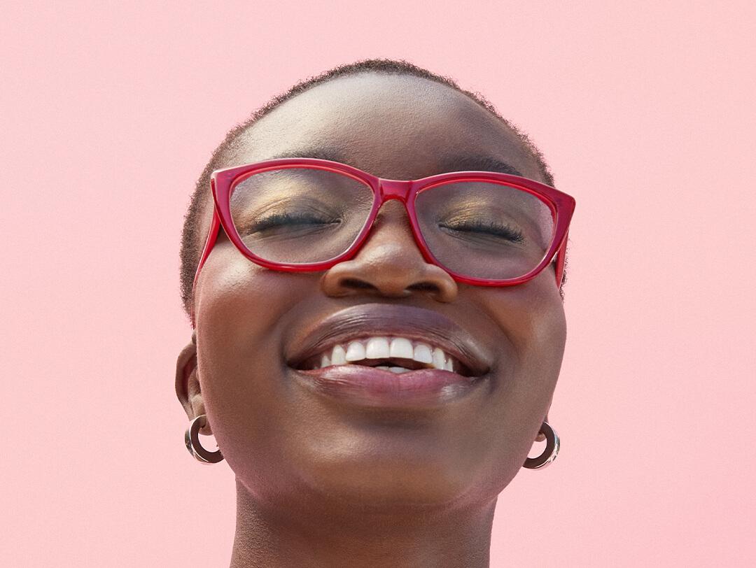 Close-up image of a model with very short hair wearing red frame eyeglasses smiling with eyes closed Desktop