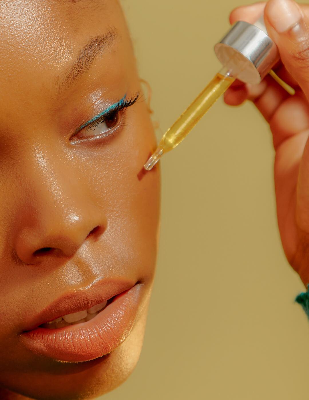 A photo of a woman wearing a colored eyeshadow putting serum on her cheeks Desktop