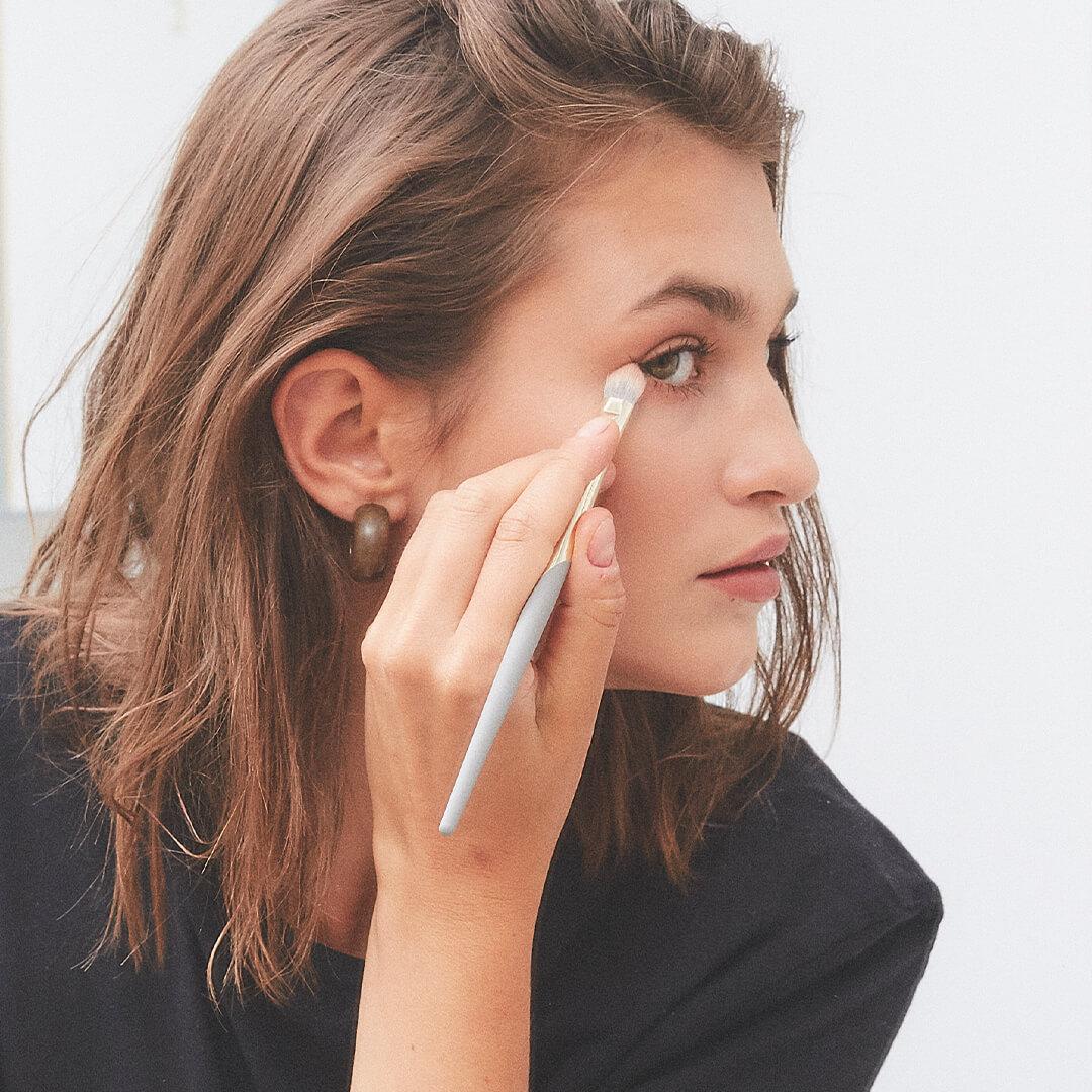 Beautiful young model in a black blouse applying eye makeup using a COMPLEX CULTURE makeup brush Mobile