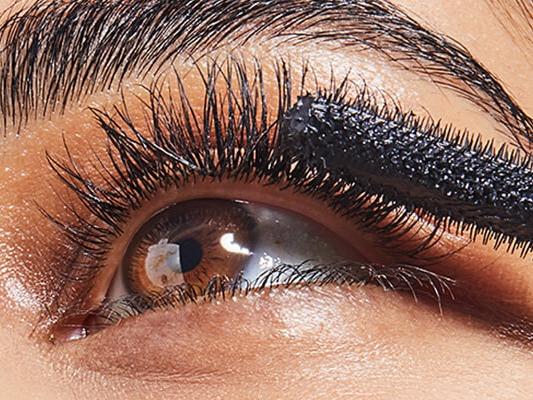 A closeup image of a model wearing neutral eyeshadow putting on mascara and an image of BRIOGEO Hair Care B. Well Organic + Cold-Pressed 100% Castor Oil Desktop