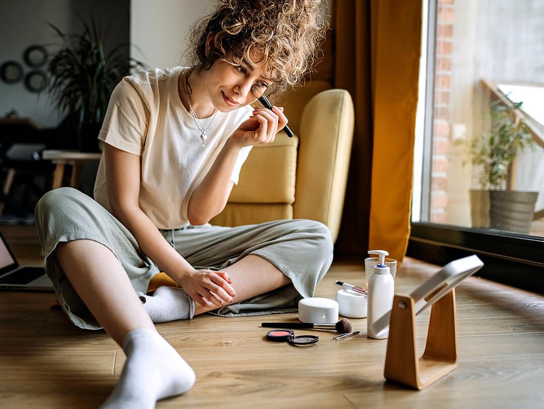 Young beautiful woman is sitting in her living room and putting on make-up Desktop