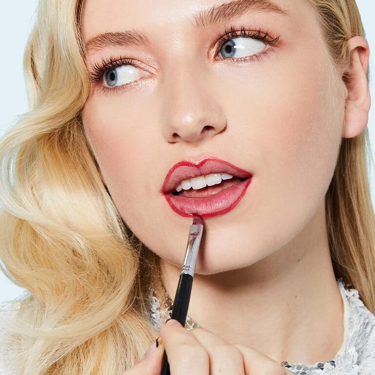 An image of a model applying lip liner using a lip brush and a closeup image of a model's red lips resting on her index finger Mobile
