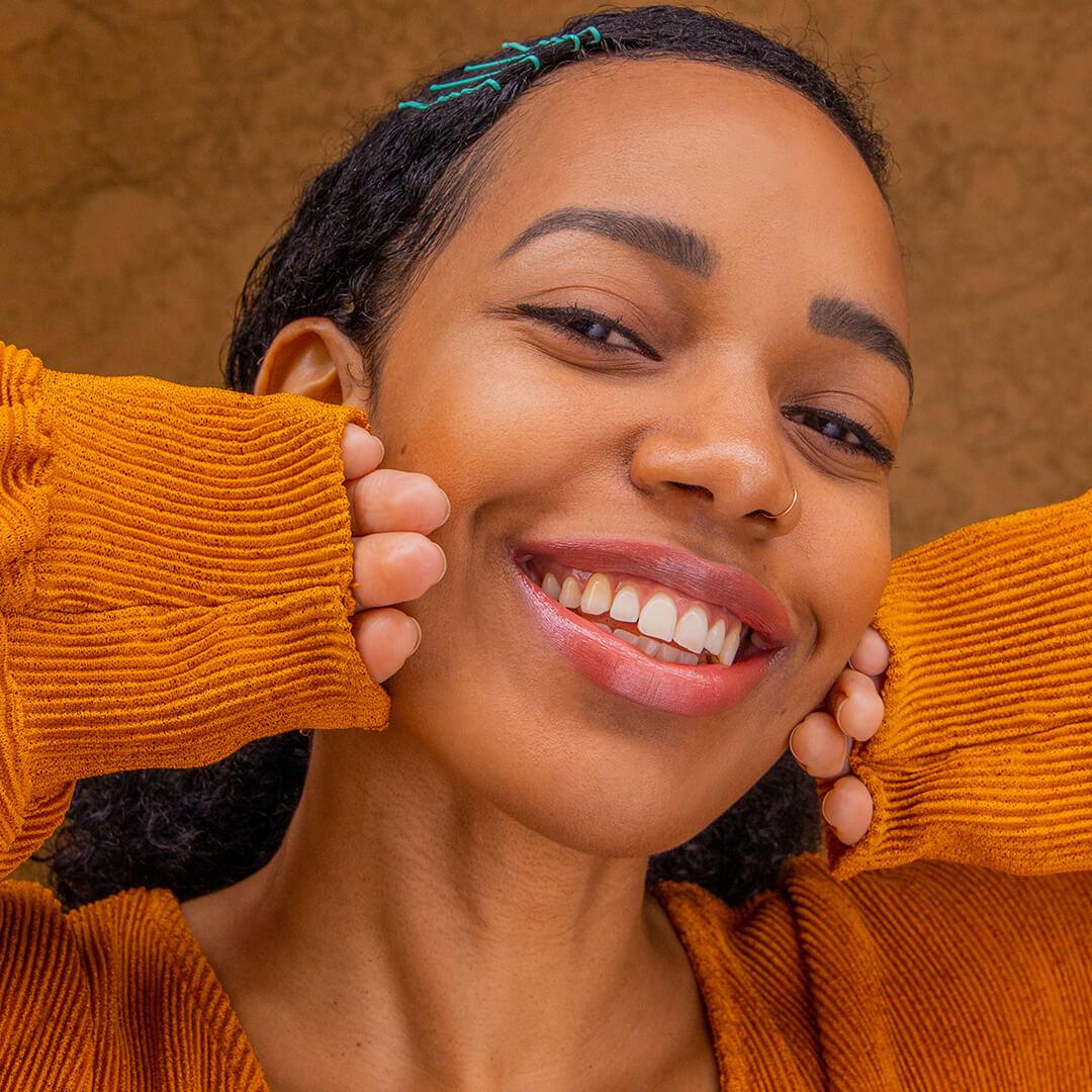 Close-up image of a smiling Bianca Alexa in a brown top paired and faux metallic nude lipstick look Mobile