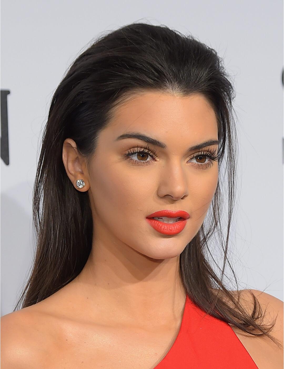 Close-up of Kendall Jenner rocking a neutral eye makeup paired with bright coral lipstick and a slicked back hairstyle Mobile