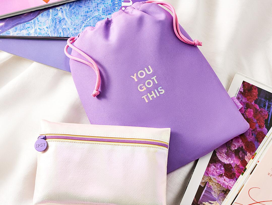 Flat lay image of September 2022 IPSY Glam Bag and Glam Bag Plus bags on white cloth with a couple of magazines Desktop