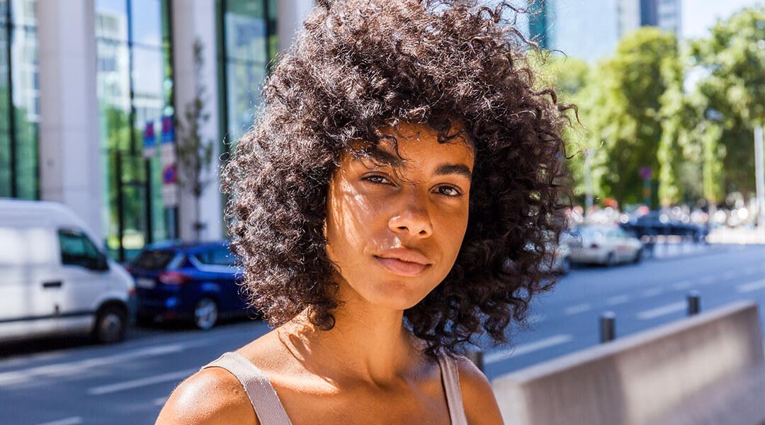 Young woman with naturally curly hair posing out in the sun on the street Desktop