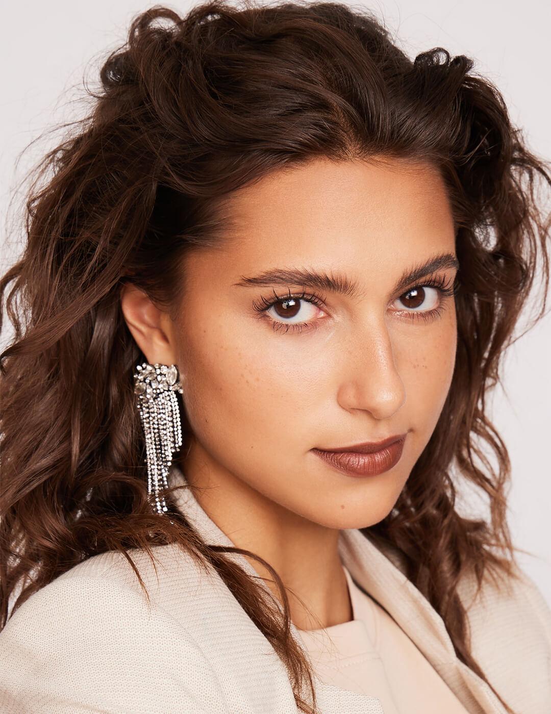 Close-up of a model rocking a wavy side part hairstyle, silver dangling earrings, and a minimal makeup look with brick red lips Mobile
