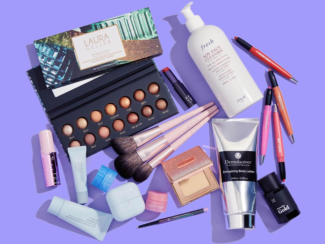 Skincare, makeup, and hair care products and tools from various brands scattered on purple background Desktop
