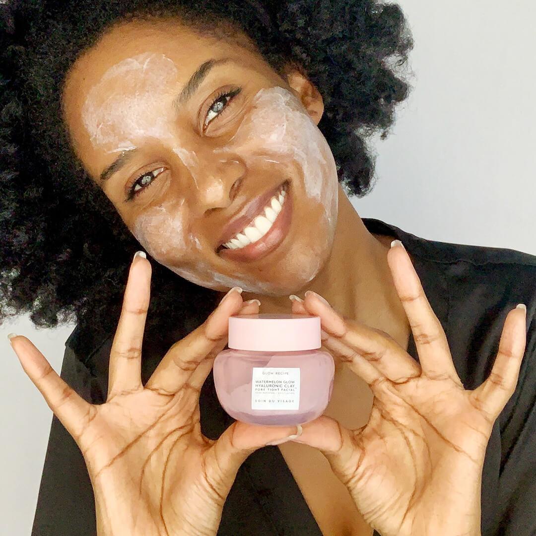 Close-up of a black woman holding the GLOW RECIPE Watermelon Glow Hyaluronic Clay Pore-Tight Facial with mask on her face Mobile