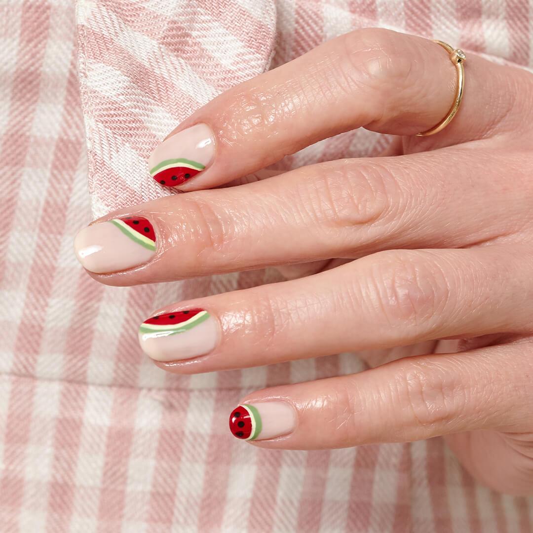 Close-up image of a hand with watermelon nail art mani against a checkered pink and white background Desktop