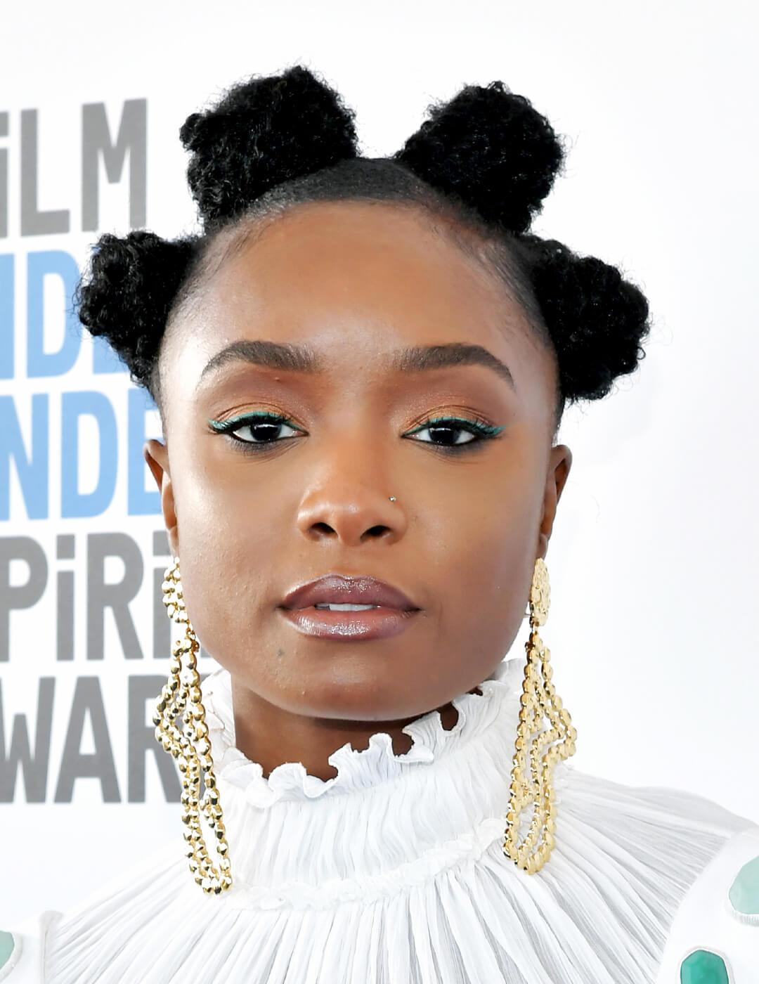 Close-up of KiKi Layne rocking a Bantu knots hairstyle and gold, dangling earrings Mobile