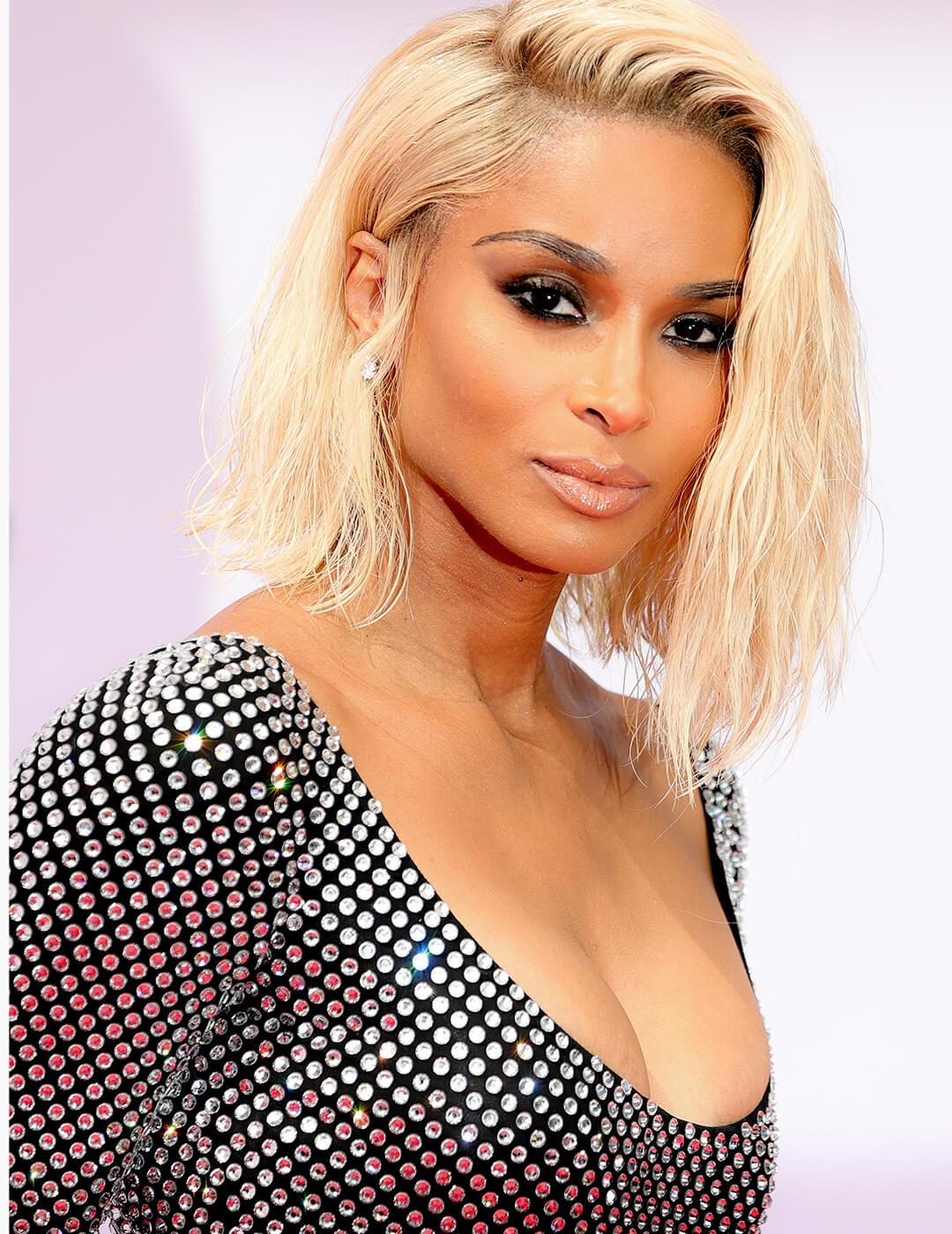 A photo of Ciara wearing a dazzling low cut dress in her mid-length blond hair tucked in her ear Mobile