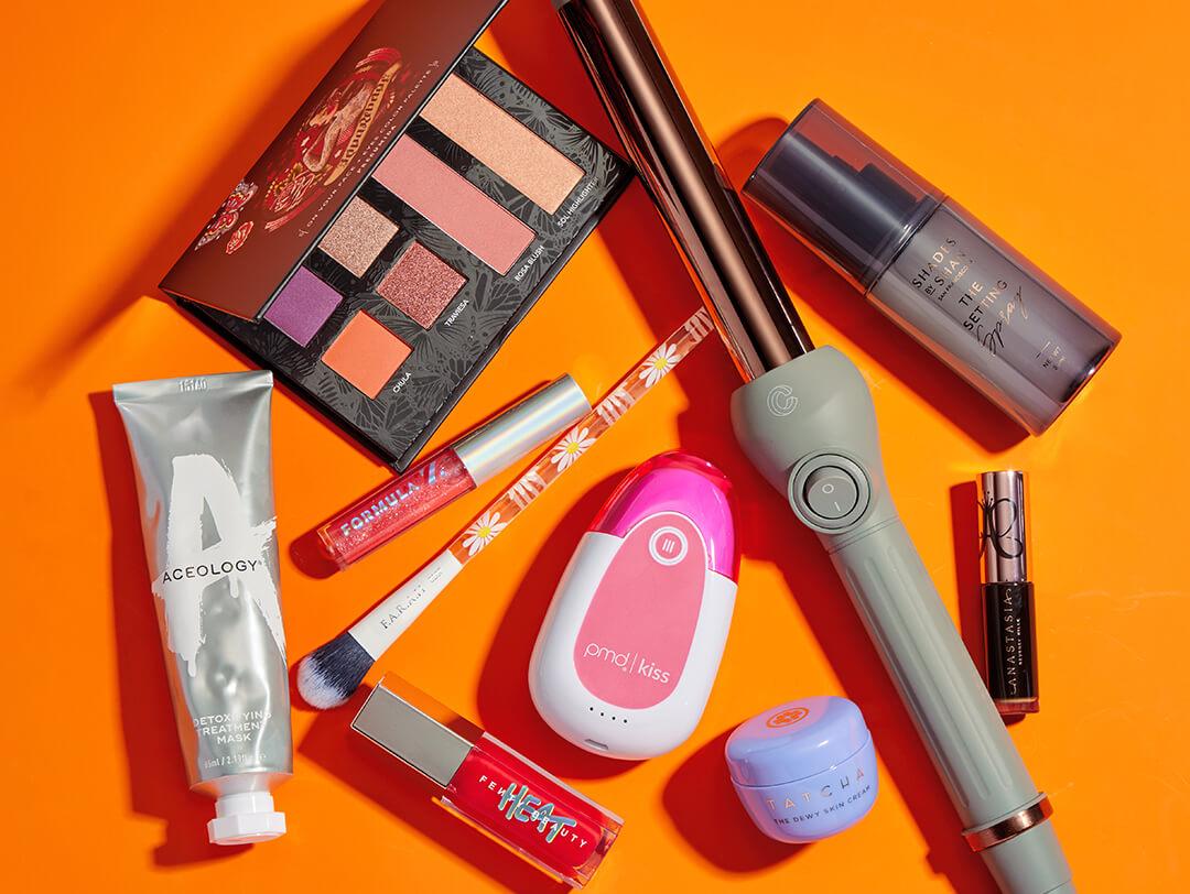 Beauty and makeup products and tools from various brands scattered on dark orange background Desktop