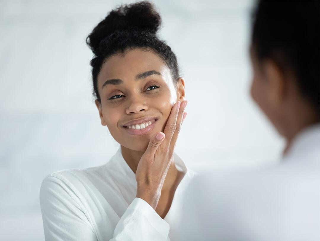 Close-up image of a Black woman touching her smooth face while checking herself in the mirror Desktop