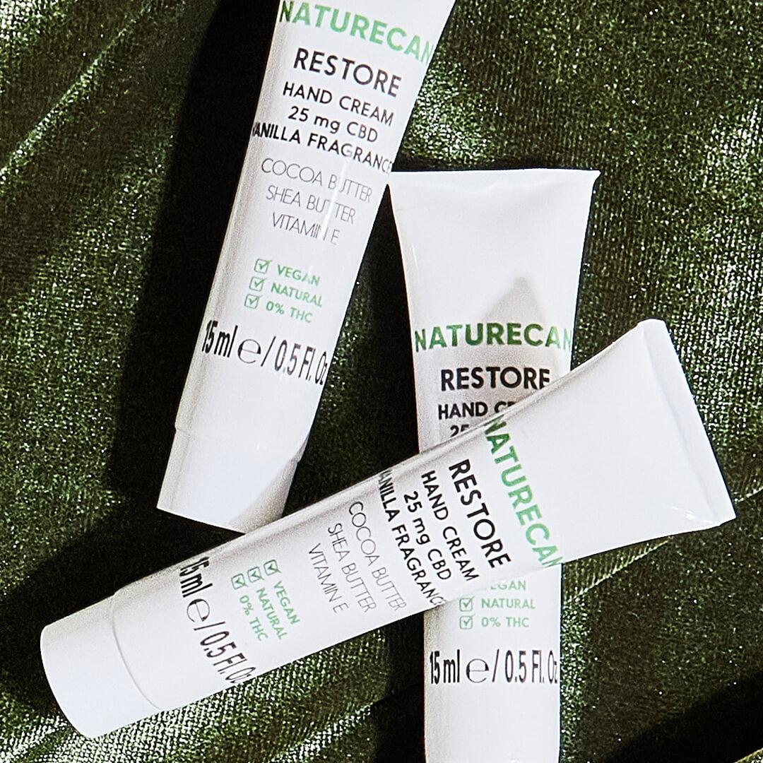 Three tubes of NATURECAN Restore CBD Hand Cream on dark green velvet cloth Mobile