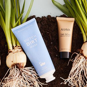A flatlay image of BLOOMEFFECTS Dutch Dirt Mask and AHAVA 24K Gold Mineral Mud Mask and orchid bulbs on dirt soil Mobile