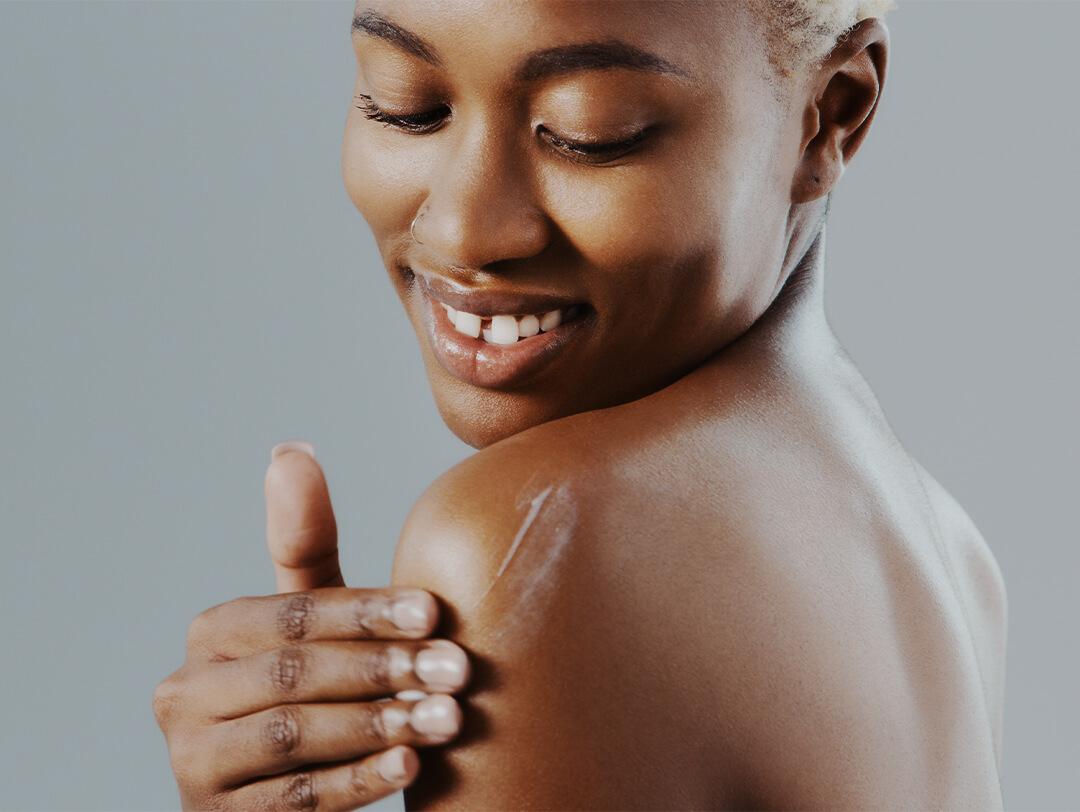 Black woman putting lotion on her shoulder Desktop