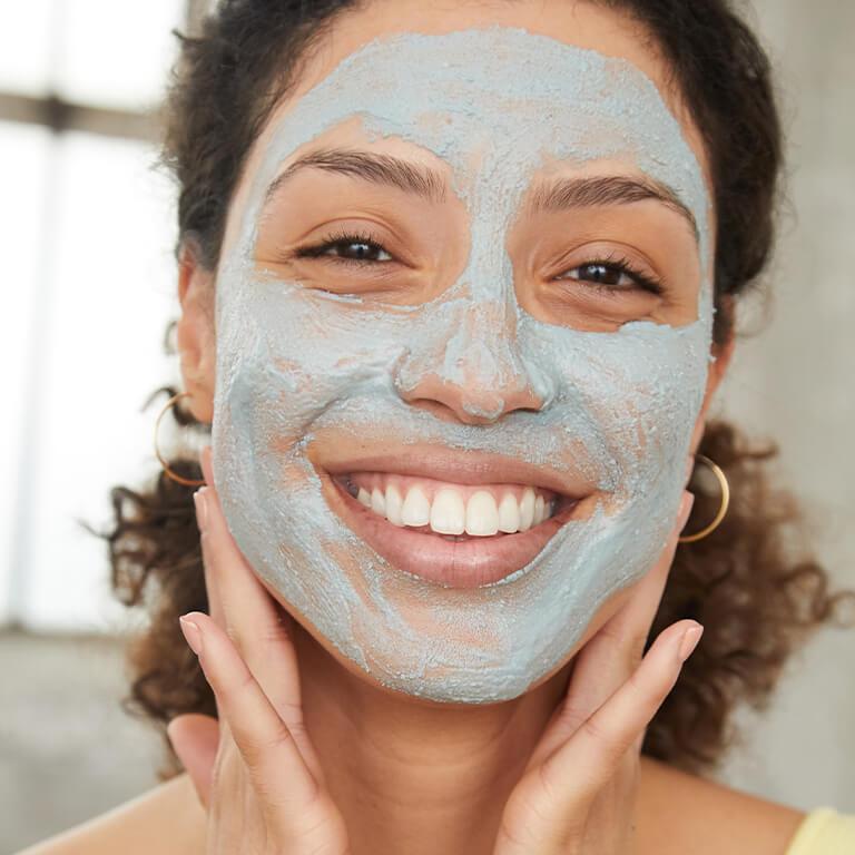 An image of a model with curly hair putting mud mask on her face Desktop