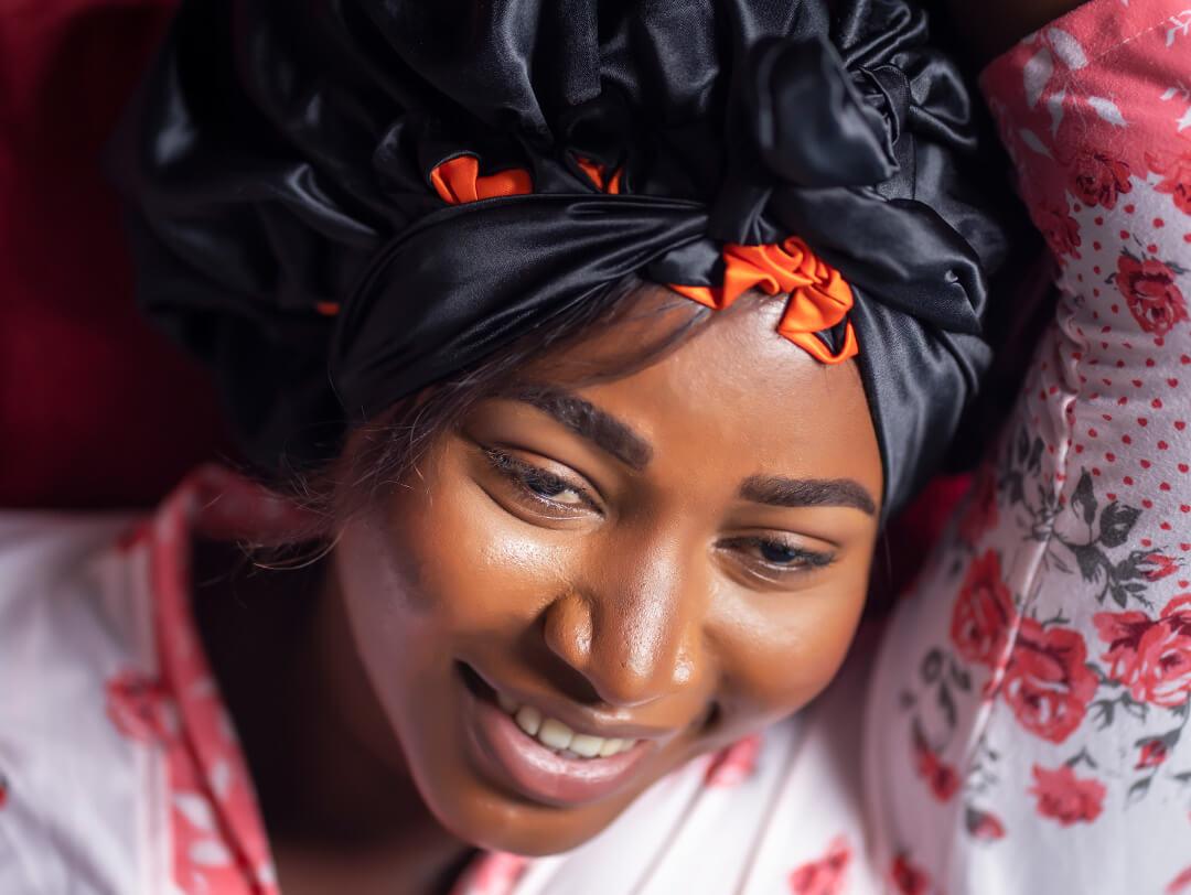 An image of woman lying on a bed, smiling, and wearing a black hair bonnet Desktop
