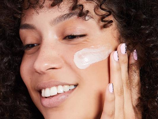 An image of a smiling model with curly hair applying cream on her cheek and an image of DERMA E Vitamin C Concentrated Serum Desktop