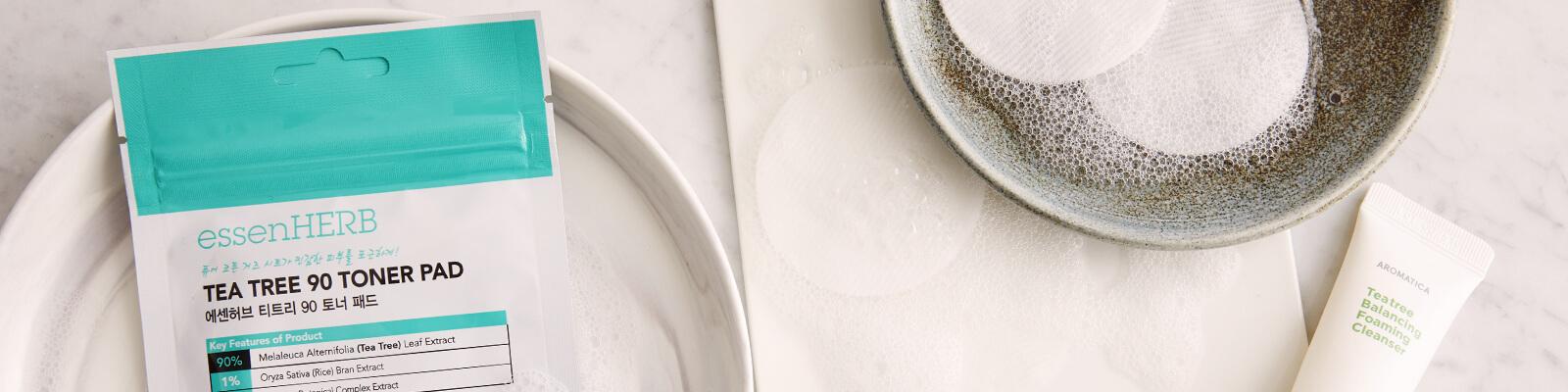 A flatlay image of tea tree oil skincare products on a marble surface Desktop
