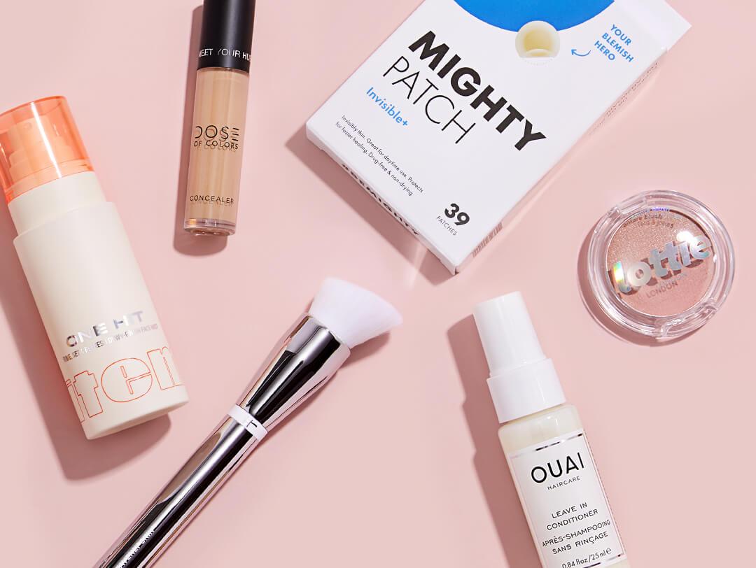 Skincare and makeup products and brush spread on pink background Desktop